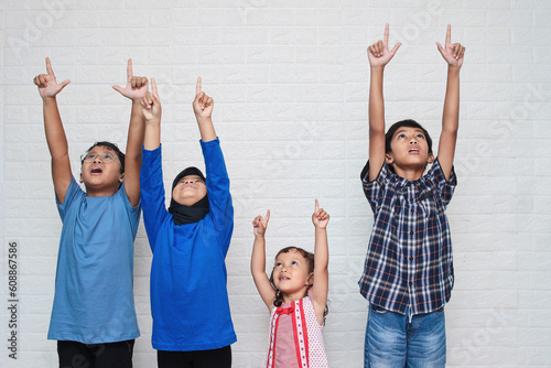 Portrait of cute Asian little kids in casual clothes looking and pointing up, isolated on a white background