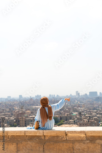 A woman in hijab sitting pointing at Cairo city in the background wallpaper