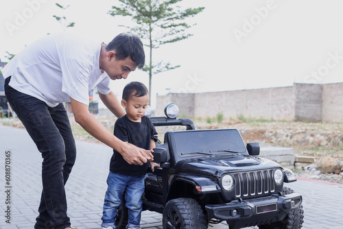 Father having fun with his son playing with big toy car at the park