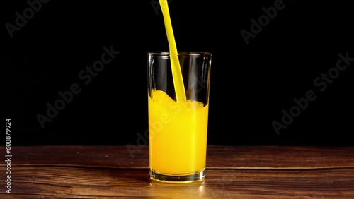 pouring fresh orange juice into aclear glass on a wooden table with a black background
