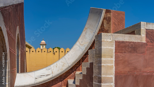 A fragment of an ancient sundial. Measuring divisions are visible on the curved white marble surface. Fortress wall against the blue sky. Jantar Mantar Observatory. India. Jaipur.