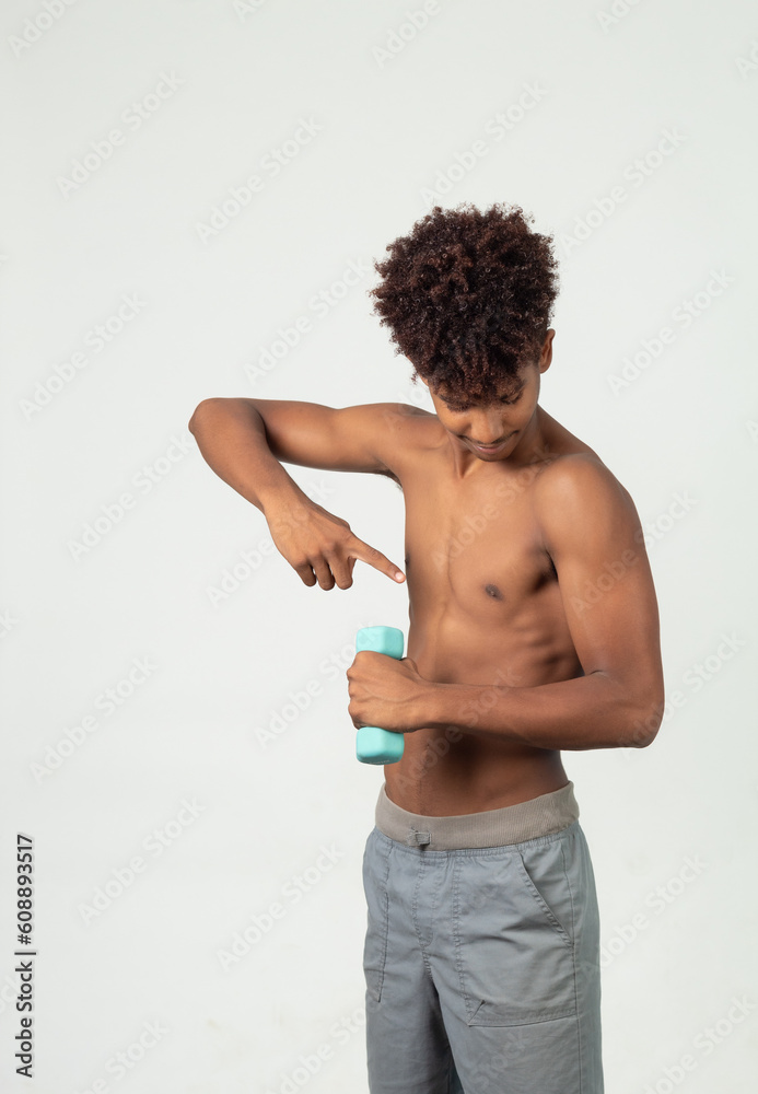 Fototapeta premium Muscular latin adolescent , teen showing his arm holding a dumbbells looking to the camera doing exercises with dumbbells isolated over white background