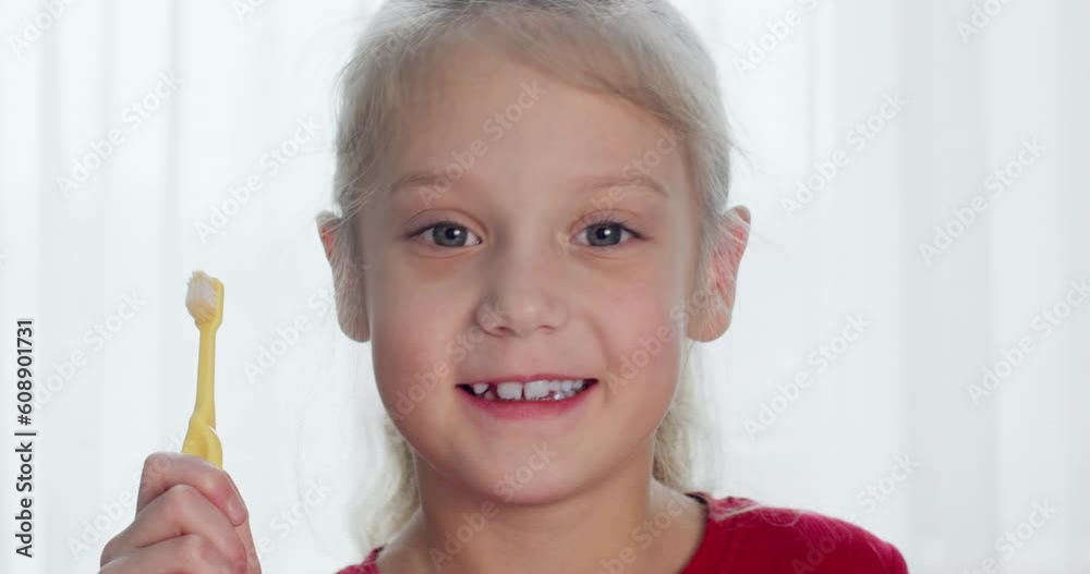 Junior schoolgirl holds yellow toothbrush in hand. Girl with fair hair and light eyes smiles and looks at camera showing fallen tooth slow motion closeup Stock Video | Adobe Stock