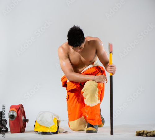 Attractive topless firefighter exudes a sense of calm and readiness as he sit and kneel down on a pristine white background showcasing his strength and preparedness.