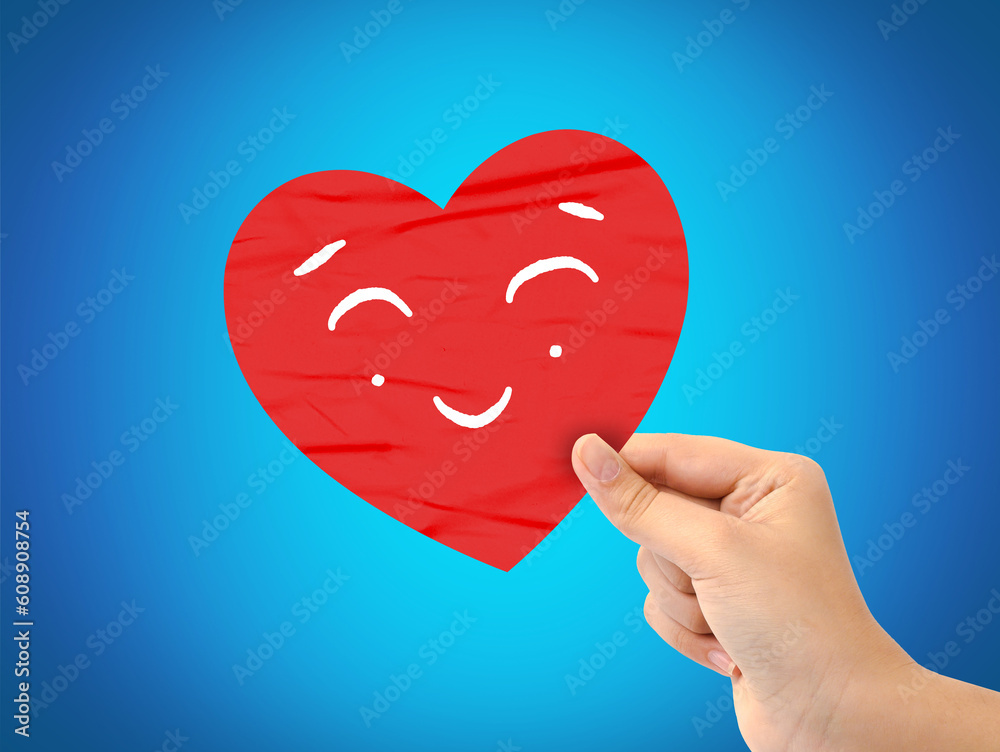 Hand holding a red Paper Smiling Heart on blue background. love concept Hand holding a red Paper Smiling Heart on blue background. love concept