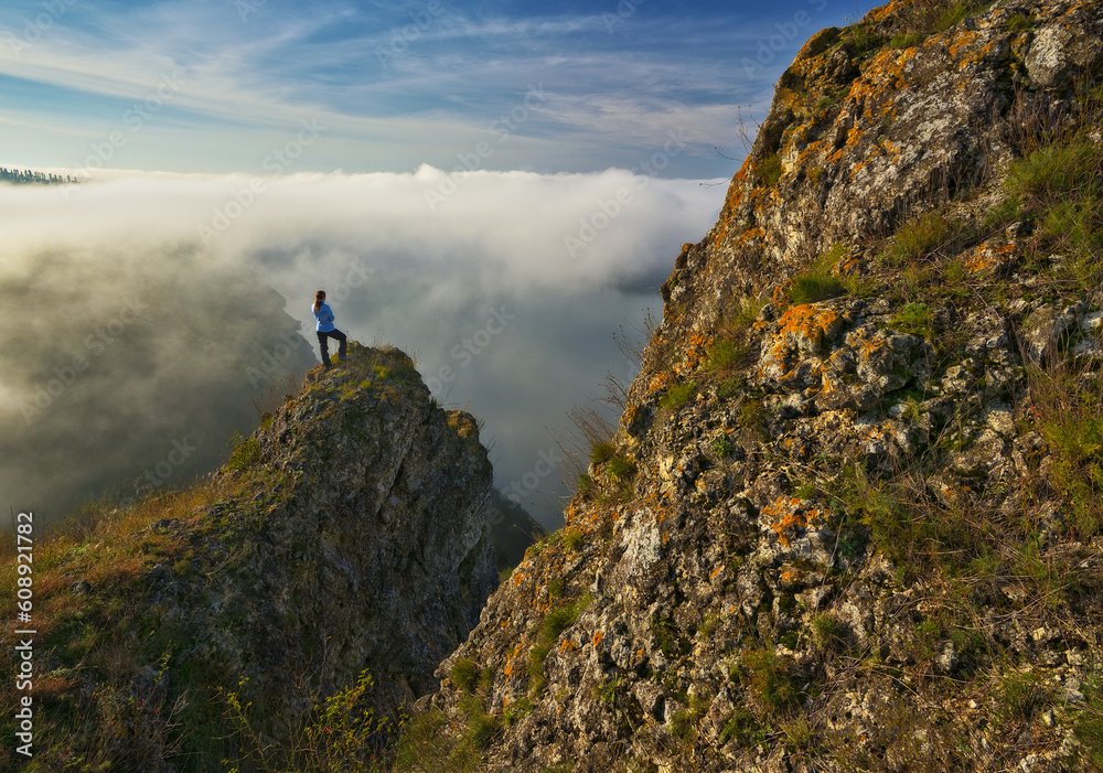 woman stands on a rock above a river canyon. female tourist enjoys foggy autumn landscape. nature of Ukraine