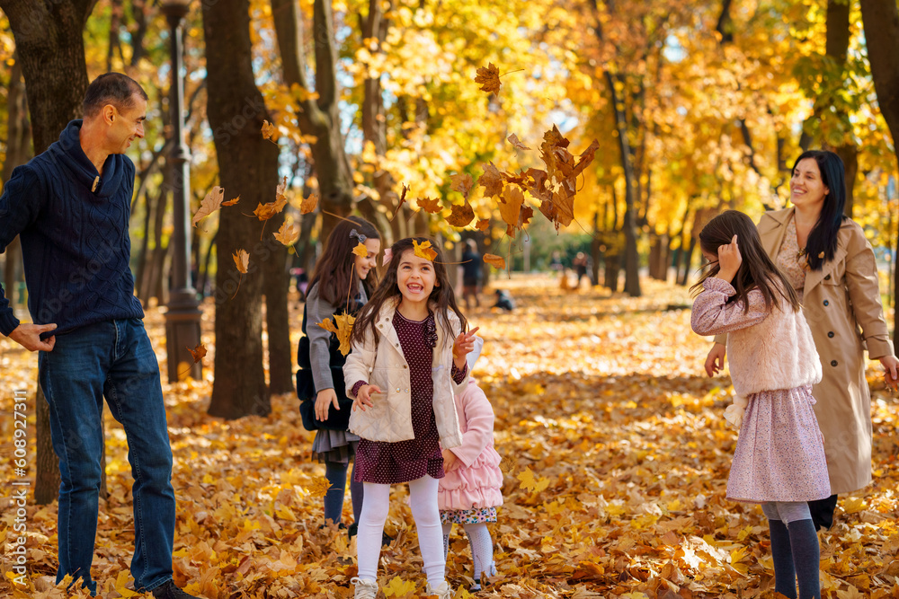 Naklejka premium portrait of a big family in autumn city park, happy parents and children playing together and throwing yellow leaves, beautiful nature, bright sunny day