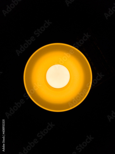 Warm orange LED lamp in the ceiling on a dark background in the center of the frame, bottom view.