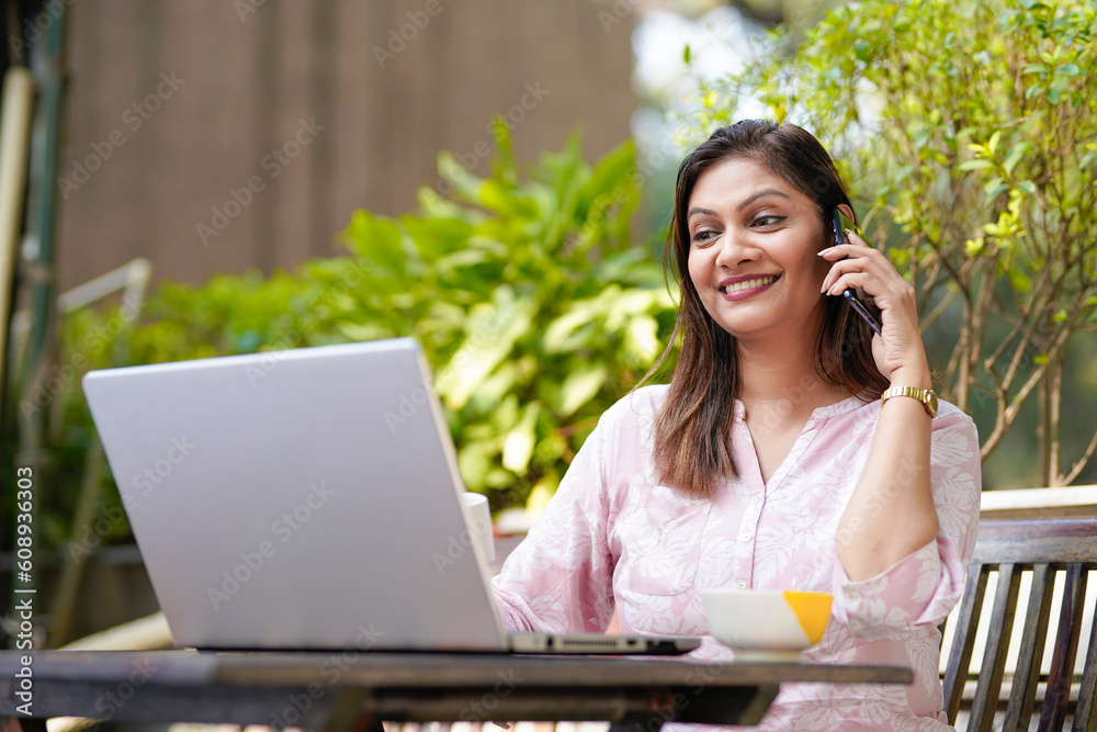 Indian woman drinking tea or coffee, using laptop and talking on smartphone. Indian woman drinking tea or coffee, using laptop and talking on smartphone.