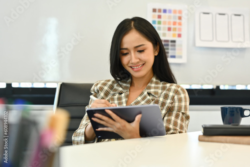 Beautiful female designer using tablet, working on mobile app development at modern workplace