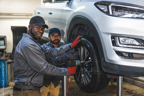 Two men auto mechanics with pneumatic wrench changing car tire on a lifted vehicle in repair shop. High quality photo © PoppyPix