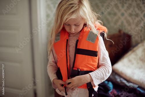Cute littel girl zipping up a life jacket at home photo