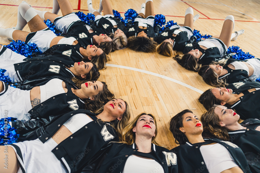 A group of cheerleaders lying on the floor forming a circle with their heads together. High quality photo