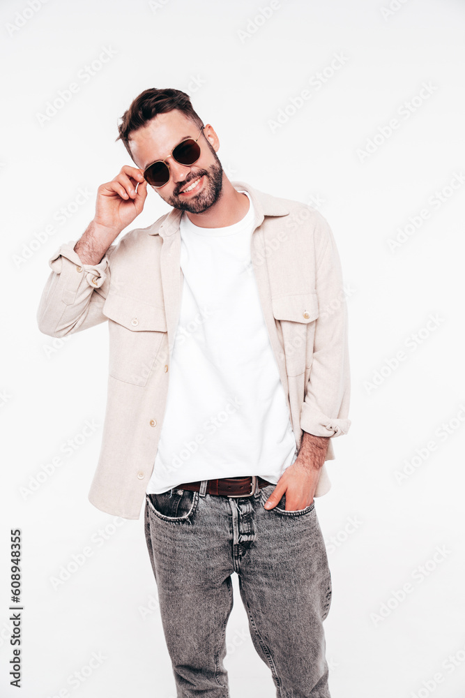 Portrait of handsome smiling stylish hipster lambersexual model. Sexy man dressed in white T-shirt and jeans. Fashion male isolated on white background in studio. In sunglasses Portrait of handsome smiling stylish hipster lambersexual model. Sexy man dressed in white T-shirt and jeans. Fashion male isolated on white background in studio. In sunglasses