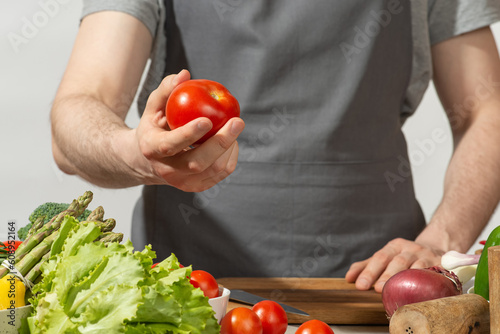 A man in a gray kitchen apron prepares a salad, close-up