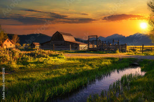 Colorful sunset over Historic John Moulton Barn at Mormon Row in Grand Teton National Park on a sunny summer day, with Teton Mountain Range in the background.