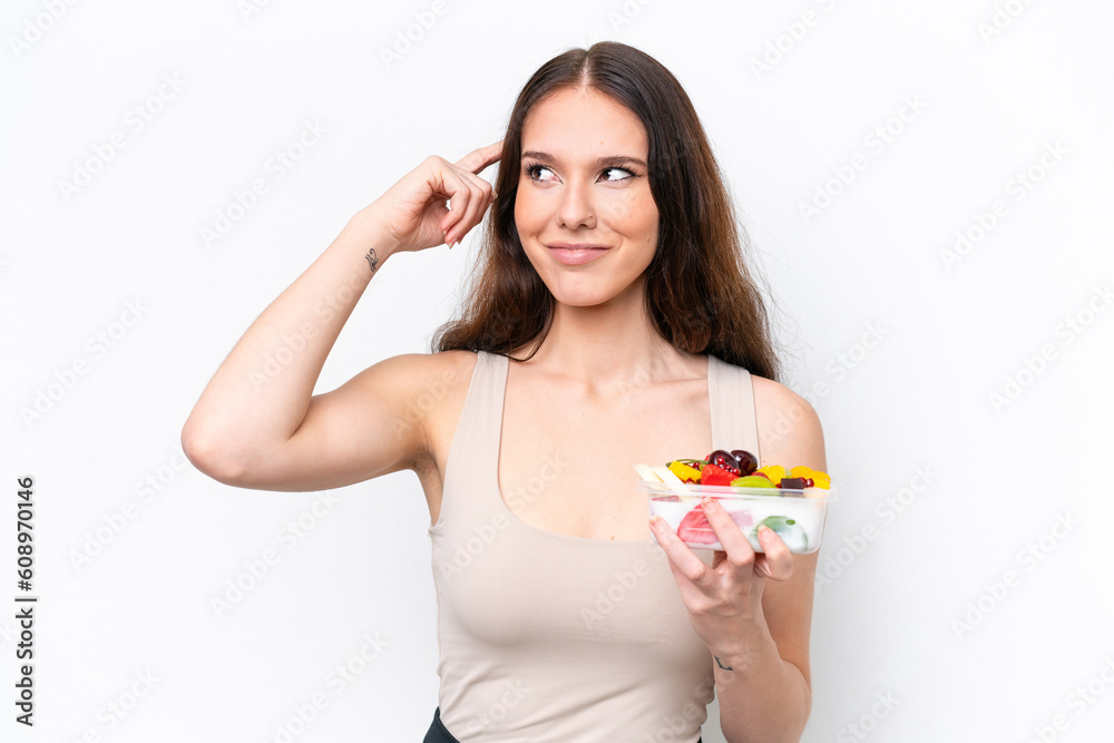 Young caucasian woman holding a bowl of fruit isolated on white background having doubts and thinking Young caucasian woman holding a bowl of fruit isolated on white background having doubts and thinking