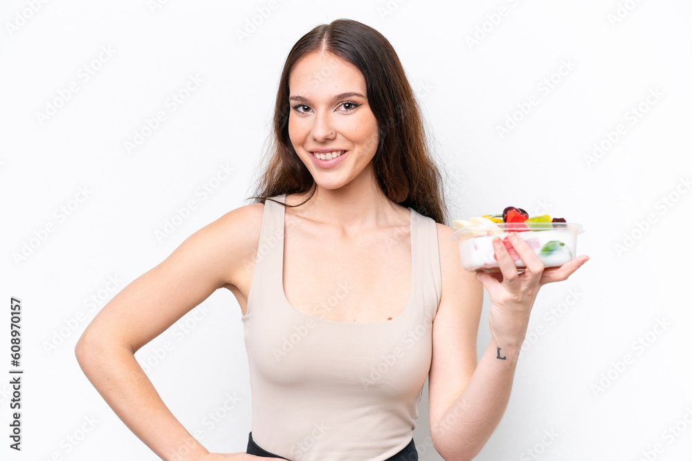 Young caucasian woman holding a bowl of fruit isolated on white background posing with arms at hip and smiling Young caucasian woman holding a bowl of fruit isolated on white background posing with arms at hip and smiling