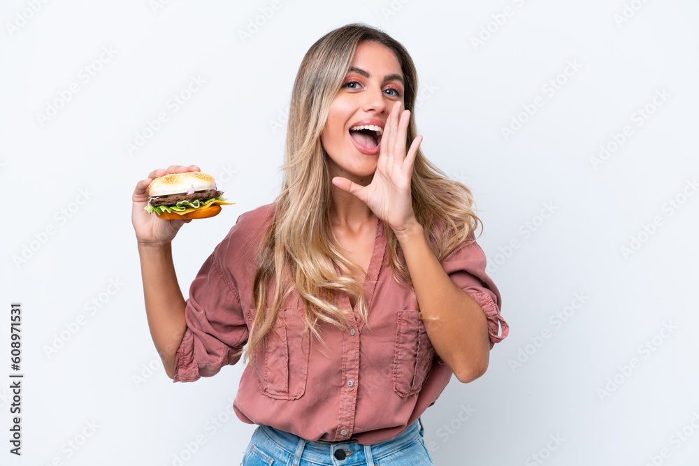 Young pretty Uruguayan woman holding a burger isolated on white background shouting with mouth wide open Young pretty Uruguayan woman holding a burger isolated on white background shouting with mouth wide open