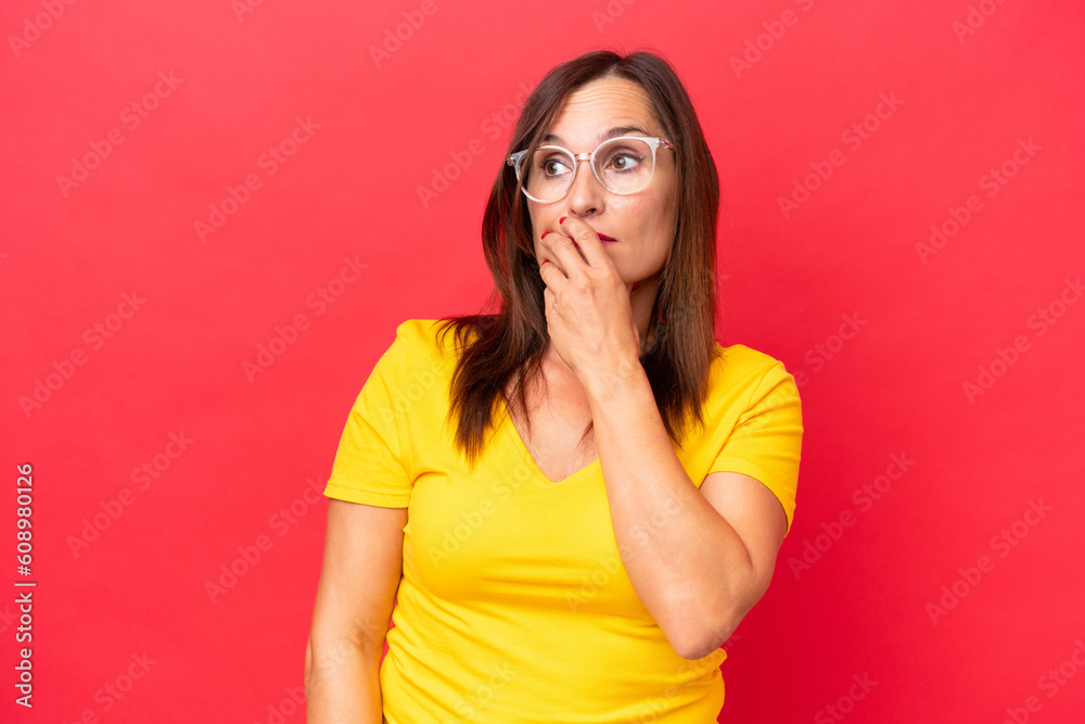 Middle-aged caucasian woman isolated on red background having doubts and with confuse face expression