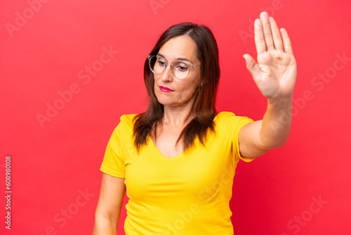 Middle-aged caucasian woman isolated on red background making stop gesture and disappointed