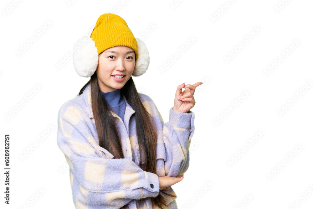 Young Asian woman wearing winter muffs over isolated chroma key background pointing finger to the side Young Asian woman wearing winter muffs over isolated chroma key background pointing finger to the side