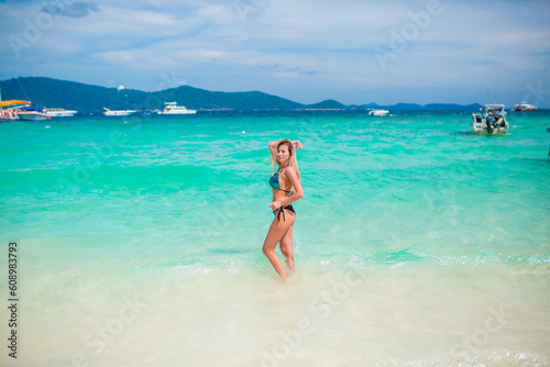 A young happy girl with a beautiful figure is standing in a bathing suit on the beach of an exotic island by the sea, a luxury resort, a concept of relaxation, vacation on a tropical beach in Thailand © Vera