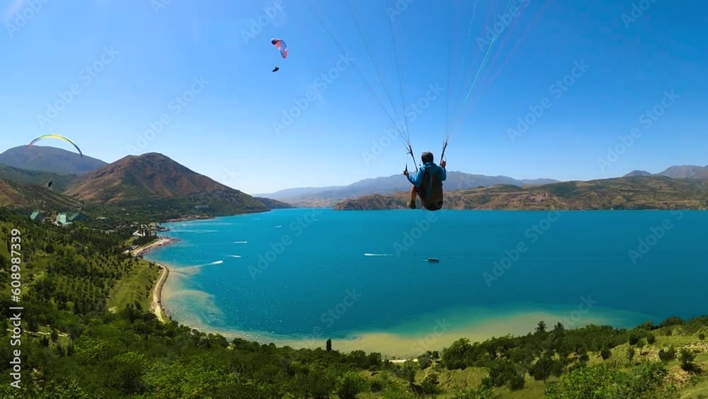 paragliding in Uzbekistan. back view from gopro man paraglider flying over the Amirsoy ski slope and Charvak lake. Extreme and active types of recreation. High quality FullHD footage