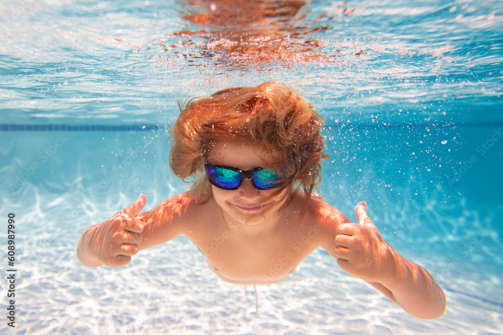 Naklejka premium Child in swimming in pool. Funny little boy swims underwater in the pool. Underwater kids portrait from under the water. Summer holiday. Kids weekend.