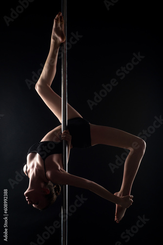 Pole dance. Sexy ballerina in black underwear stretching on black background. Concept of ballet art. Sexy pole dancer. Beautiful sexy fitness girl with great figure flexing her perfect body