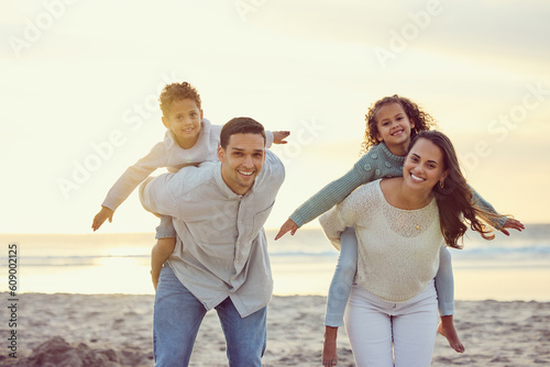 Portrait of parents piggyback kids on beach for family holiday, summer vacation and weekend. Nature, travel and happy mother, father and children playing by ocean for bonding, fun and quality time #609002125