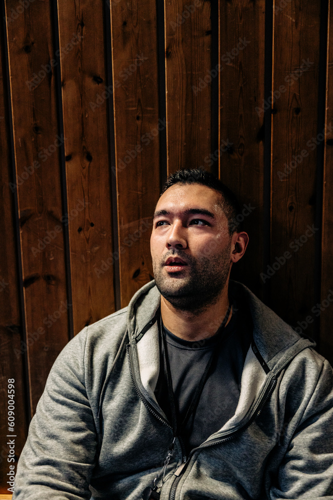 Male athlete looking away while sitting near wooden wall Male athlete looking away while sitting near wooden wall
