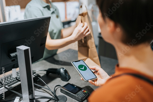 Female customer scanning credit card reader while paying through mobile phone in electronics store photo