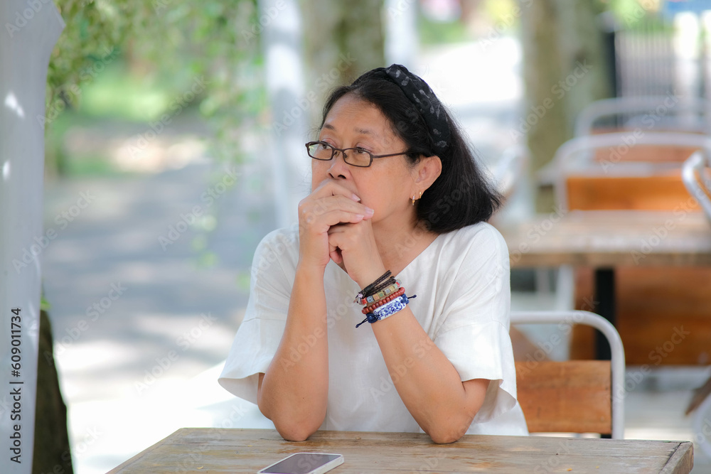 Fototapeta premium Woman sitting alone on garden table looking bored waiting for her meal she ordered from the restaurant