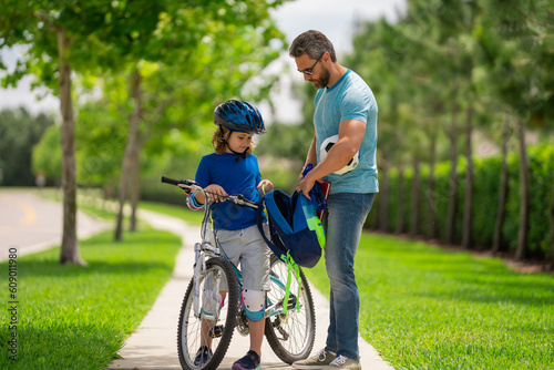 Father and son concept. Father teaching son riding bike. Father helping son to ride a bicycle in american neighborhood. Child in safety helmet learning to ride cycle with his dad. Fathers day.
