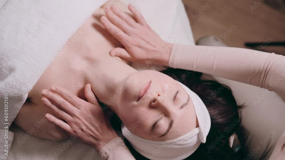 The beautician makes a facial massage. Young woman lies on her back and gets a facelift in a spa salon. Massage techniques for anti-aging. The beautician makes a facial massage. Young woman lies on her back and gets a facelift in a spa salon. Massage techniques for anti-aging.