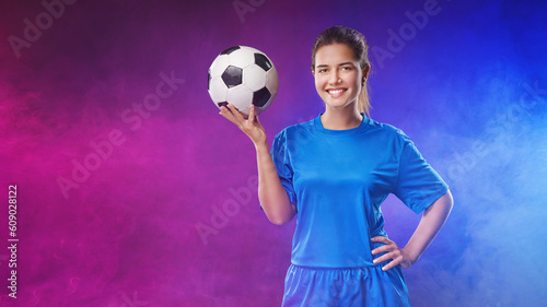  Portrait of young smiling female soccer player with soccer ball standing in the colorful neon light.