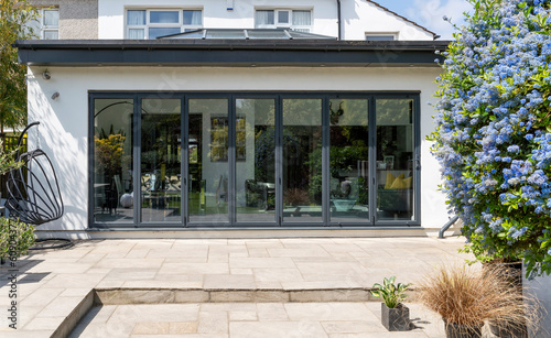 Stylish, closed, bifold doors with plants in spring, summer, revealing interior of a designer, lifestyle, kitchen diner room and indian sandstone patio.
