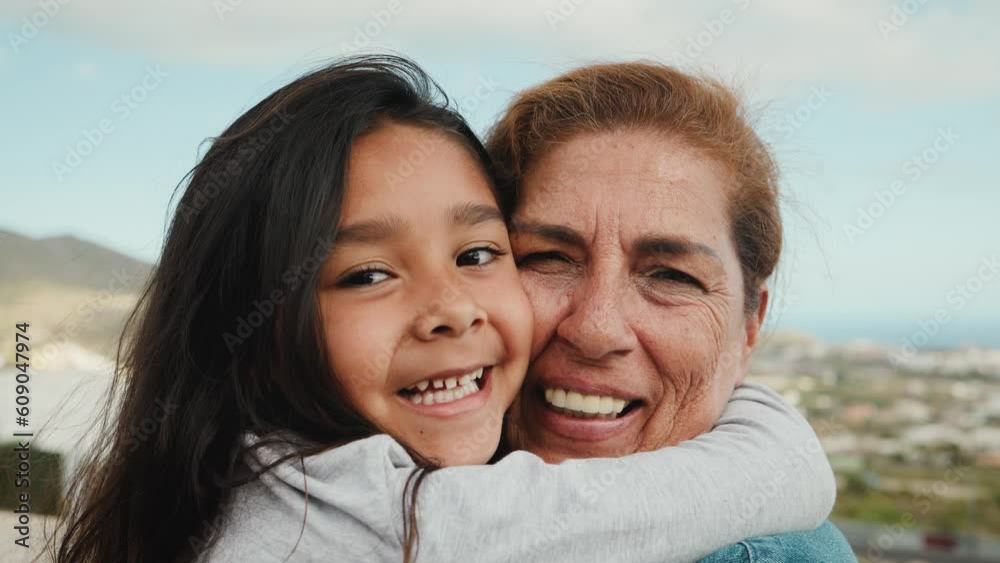 Happy Hispanic child enjoying time with grandmother smiling in front of camera at house rooftop Happy Hispanic child enjoying time with grandmother smiling in front of camera at house rooftop