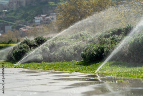 Automatic sprinkler system watering the lawn. Irrigation for plants in public park and city centre. Watering grass for fresh growth. Moisturising cleansing air hygiene. Eco friendly, healthy, wellness photo