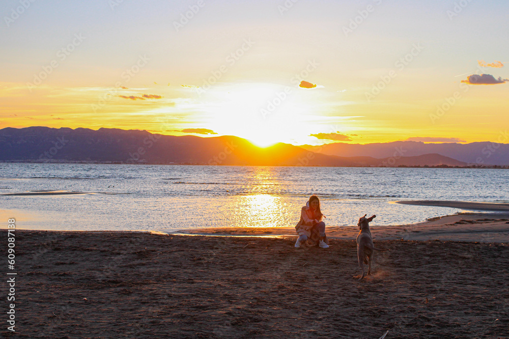 girl playing with dog on the beach at sunset