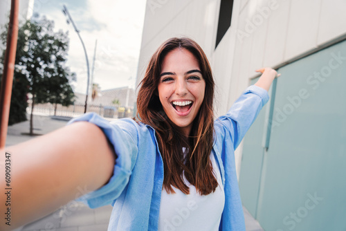 Obraz na plátne Happy young caucasian student lady looking at camera and taking a selfie portrait having fun, standing outside