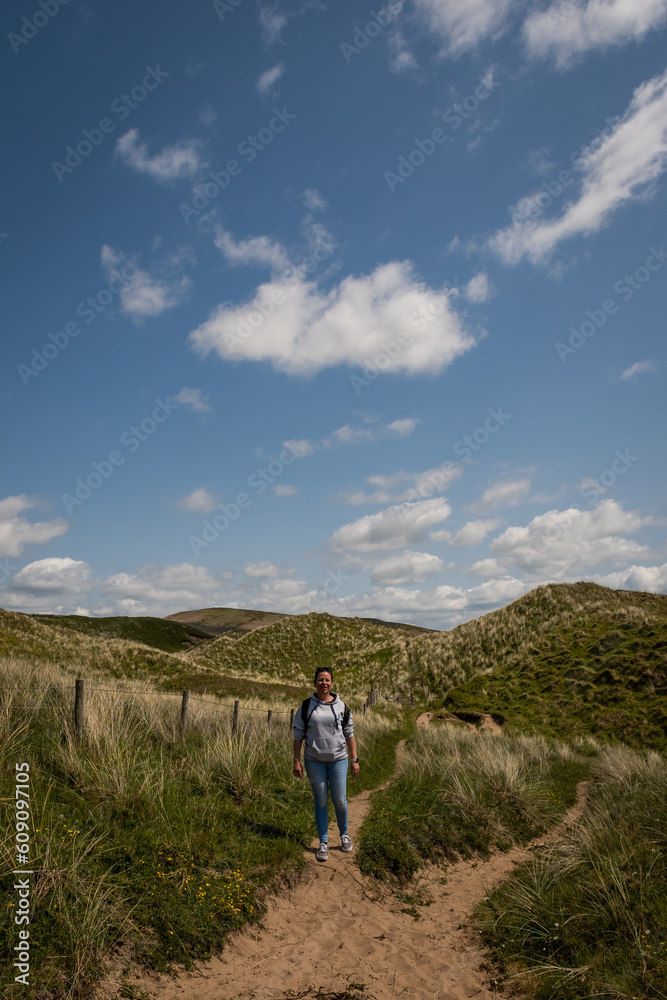 Active outdoor lifestyle in the British coastal countryside. young lady embraces the great outdoors in the Gower peninsular trekking over grassy sand dunes to get to Rhossili beach on a sunny day