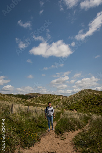 Active outdoor lifestyle in the British coastal countryside. young lady embraces the great outdoors in the Gower peninsular trekking over grassy sand dunes to get to Rhossili beach on a sunny day © drew