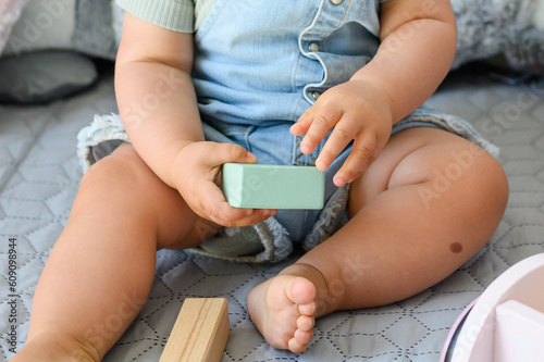 Crop baby playing with toy block on bed