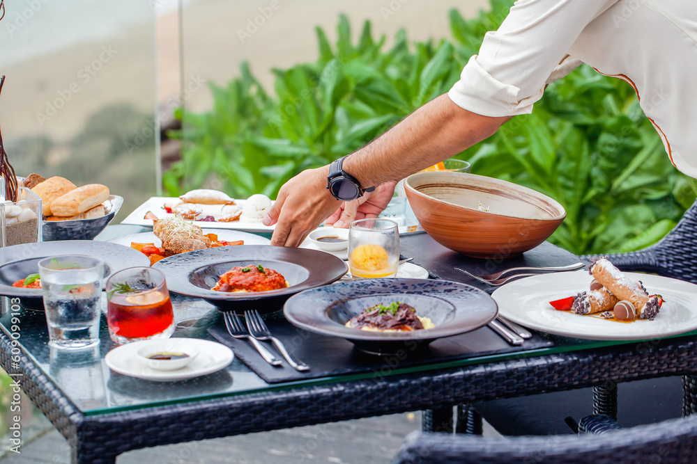 At a seaside restaurant, a waiter serves a table overlooking the ocean, providing a perfect setting for guests to enjoy a meal during their beach holiday. Gourmet food, fine dining experience At a seaside restaurant, a waiter serves a table overlooking the ocean, providing a perfect setting for guests to enjoy a meal during their beach holiday. Gourmet food, fine dining experience
