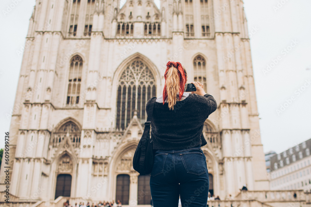 woman wearing a red kerchief taking a photo of a cathedral