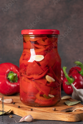 Fototapeta Pickled sweet peppers with garlic in glass jar on brown background, Vertical for