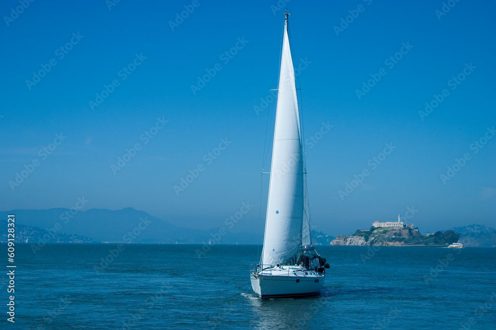 A sailboat cruises on San Francisco Bay as Alcatraz prison looms in the background.