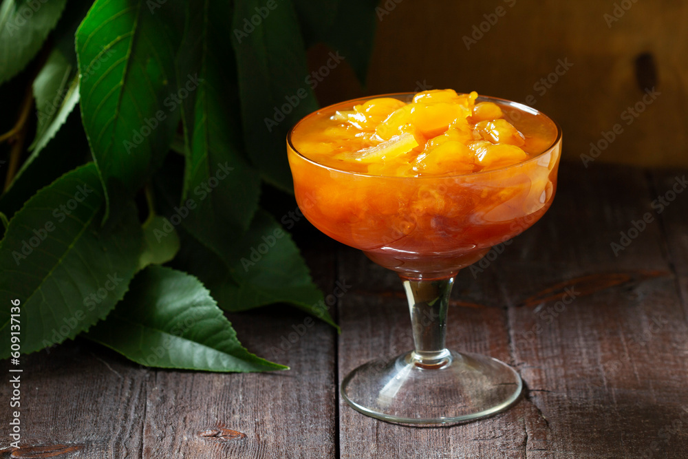 Yellow cherry jam with lemon and vanilla in a glass bowl on a wooden background.